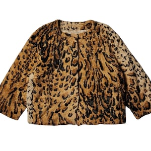 May include: A short-sleeved jacket with a leopard print pattern. The jacket features a round neckline and a button closure. The colors include shades of brown, tan, and black, creating a classic animal print design.