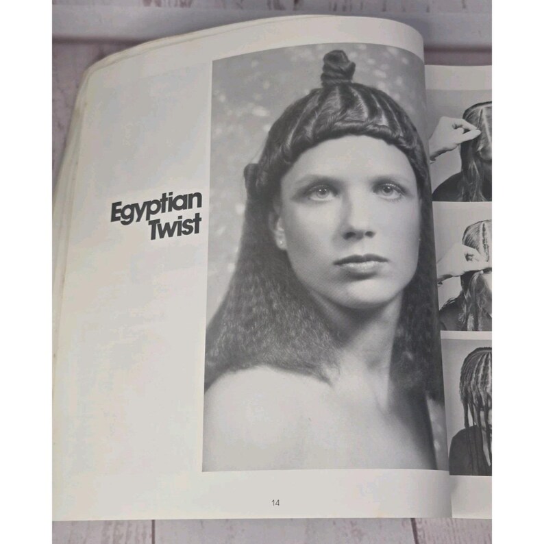 以下が含まれることがあります： ヴィンテージのヘアスタイリングブックからの白黒画像。ページには、「Egyptian Twist」とラベル付けされた凝ったヘアスタイルを持つ人物の肖像画が掲載されています。追加の小さな画像は、スタイリングプロセスを示しています。番号14が下部に表示されます。