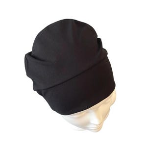 May include: A black beanie hat with a folded brim, displayed on a white mannequin head. The hat is made of a soft, dark fabric. The beanie is a simple, yet stylish accessory.