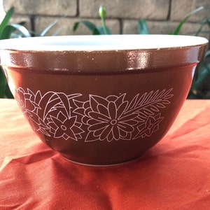 Puede incluir: Un tazón mezclador marrón con un diseño floral blanco. El tazón tiene un interior blanco y un exterior marrón.