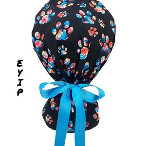 eyip ponytail scrub cap for women with long hair made of 100% cotton fabric featuring floral dog paw prints on a black background it comes with clear buttons for mask & blue grosgrain ribbon perfect surgical hat for healthcare workers
