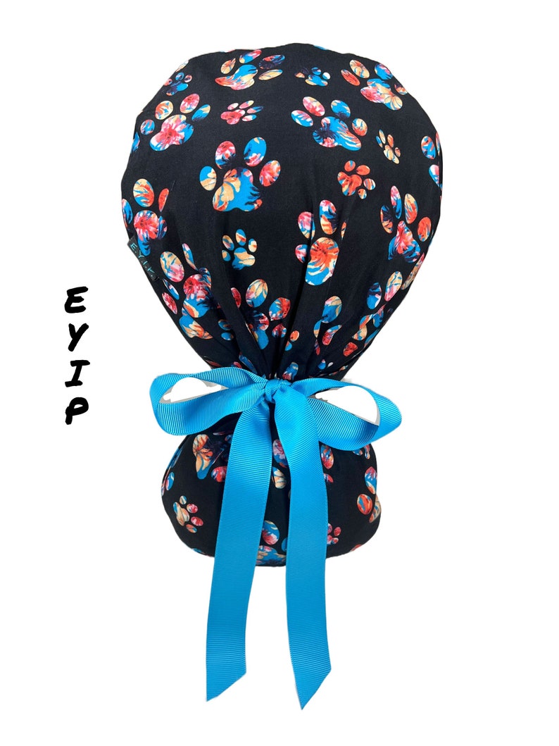 eyip ponytail scrub cap for women with long hair made of 100% cotton fabric featuring floral dog paw prints on a black background it comes with clear buttons for mask & blue grosgrain ribbon perfect surgical hat for healthcare workers