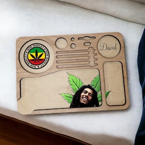 May include: Wooden rolling tray featuring a Bob Marley logo, a portrait of Bob Marley, and the name "David" engraved on the side. The tray has a compartment for rolling papers, a grinder, and a small compartment for other items.