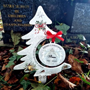 May include: White Christmas tree ornament with a red ribbon and a white circle with the text "Merry Christmas" and "Mum 1957-2020".