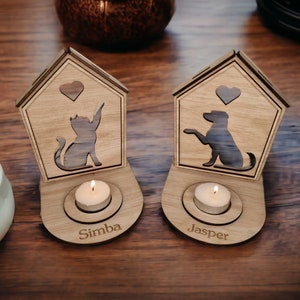 Op de afbeelding: Twee houten kaarshouders met een kat en hond silhouet, elk met een theelichtje en een gepersonaliseerde naam, "Simba" en "Jasper".