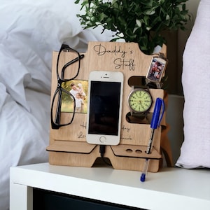May include: Wooden organiser with the words "Daddy's Stuff" engraved on it. It has slots for a phone, glasses, a watch, a pen, and a key chain. There are also two small photo slots.