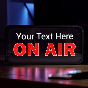 May include: Black rectangular sign with white text that says "Your Text Here" and red text that says "ON AIR".