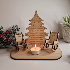 Könnte beinhalten: Weihnachtsbaum-Anhänger aus Holz mit zwei Schaukelstühlen und einer Kerze. Die Stühle sind mit "Grandpa" und "Grandma" graviert. Der Baum trägt den Text "Christmas in heaven what do they do? They come down to earth to spend it with you. So save them a seat just one empty chair. You may not see them but they will be there."
