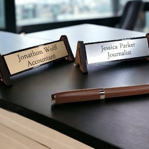 May include: Two desk nameplates with black stands. The top nameplate is gold with the text "Jonathon Wolff Accountant". The bottom nameplate is silver with the text "Jessica Parker Journalist".