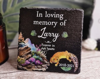 May include: Black slate memorial plaque with a white inscription that reads "In loving memory of Larry Forever in our hearts 2018-2021". The plaque features a colorful illustration of a lizard and foliage.