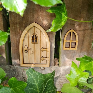 Könnte beinhalten: Eine Holztür für Feen mit einem kleinen Fenster und einem Schlüsselloch, befestigt an einem Holzzaun mit grünem Efeu, der darum wächst.