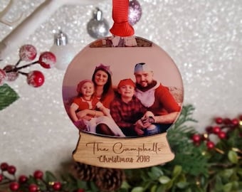 May include: A personalized Christmas ornament featuring a family photo inside a clear glass globe. The base is made of wood and has the text "The Campbells Christmas 2018" engraved on it.