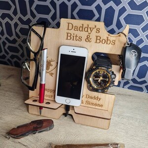 May include: A wooden desk tidy with the text "Daddy's Bits & Bobs" and "Happy our Daddy & Simone". It holds a phone, watch, keys, glasses, pen, knife, and a cigar.