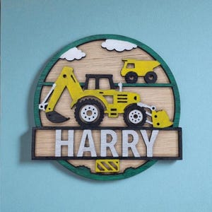 Könnte beinhalten: Wanddekoration im Baustil aus Holz mit einem gelben Bagger und Muldenkipper. Das Design beinhaltet den Namen "HARRY" in silbernen Buchstaben, vor einem Holzgrund mit grünem Rand und weißen Wolken.