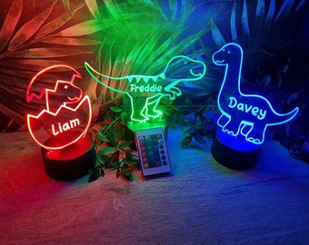 May include: Three illuminated dinosaur-shaped night lights with personalized names: "Liam", "Freddie", and "Davey". Each light sits on a black base and emits a vibrant glow. A remote control is visible, offering color customization for these decorative, kid-friendly lamps.