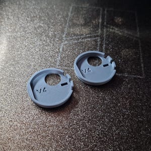 Pode incluir: Dois pequenos componentes circulares azul claro impressos em 3D com um orif&iacute;cio central e duas ranhuras. Cada componente tem o n&uacute;mero "14" impresso. Os componentes est&atilde;o sobre uma superf&iacute;cie escura texturizada.