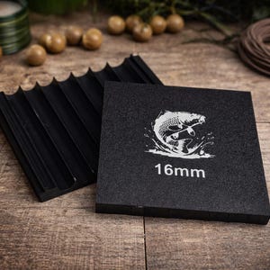 May include: Black square with a white graphic of a fish jumping out of water, and the text "16mm". A black, ridged object is next to the square. The objects are on a wooden surface.