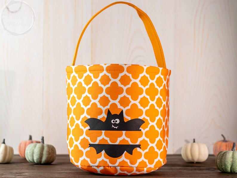 May include: Orange and white patterned Halloween treat bag with a black bat design. The bag has an orange handle and is surrounded by small pumpkins. A festive container for trick-or-treating.
