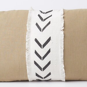 May include: A tan linen pillow with a white fringe trim and black chevron pattern.