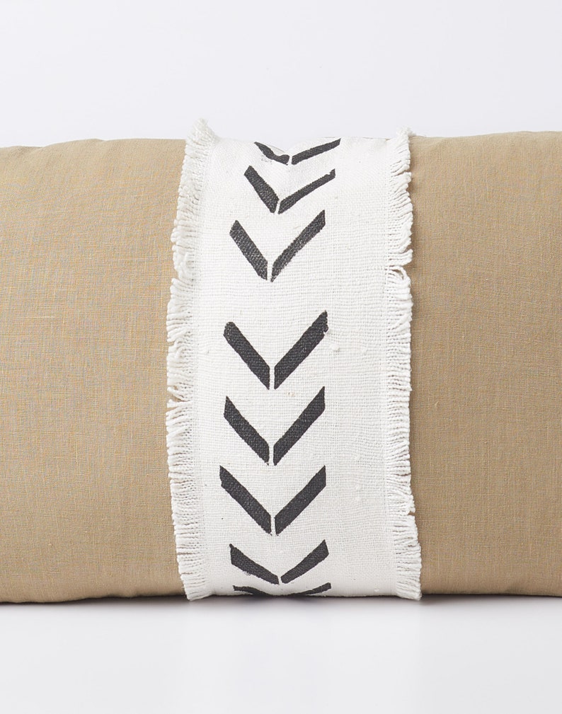 May include: A tan linen pillow with a white fringe trim and black chevron pattern.