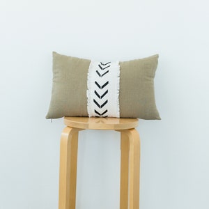 May include: A light brown throw pillow with a white and black chevron pattern on the front. The pillow is sitting on a wooden stool.