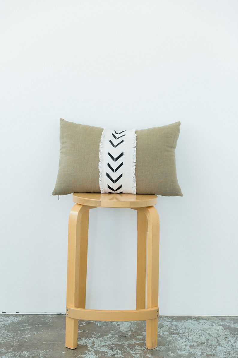 May include: A light brown throw pillow with a white and black chevron pattern on the front. The pillow is sitting on a wooden stool.