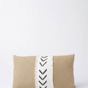 May include: A beige rectangular pillow with a white and black chevron pattern down the center. The pillow has a frayed edge.