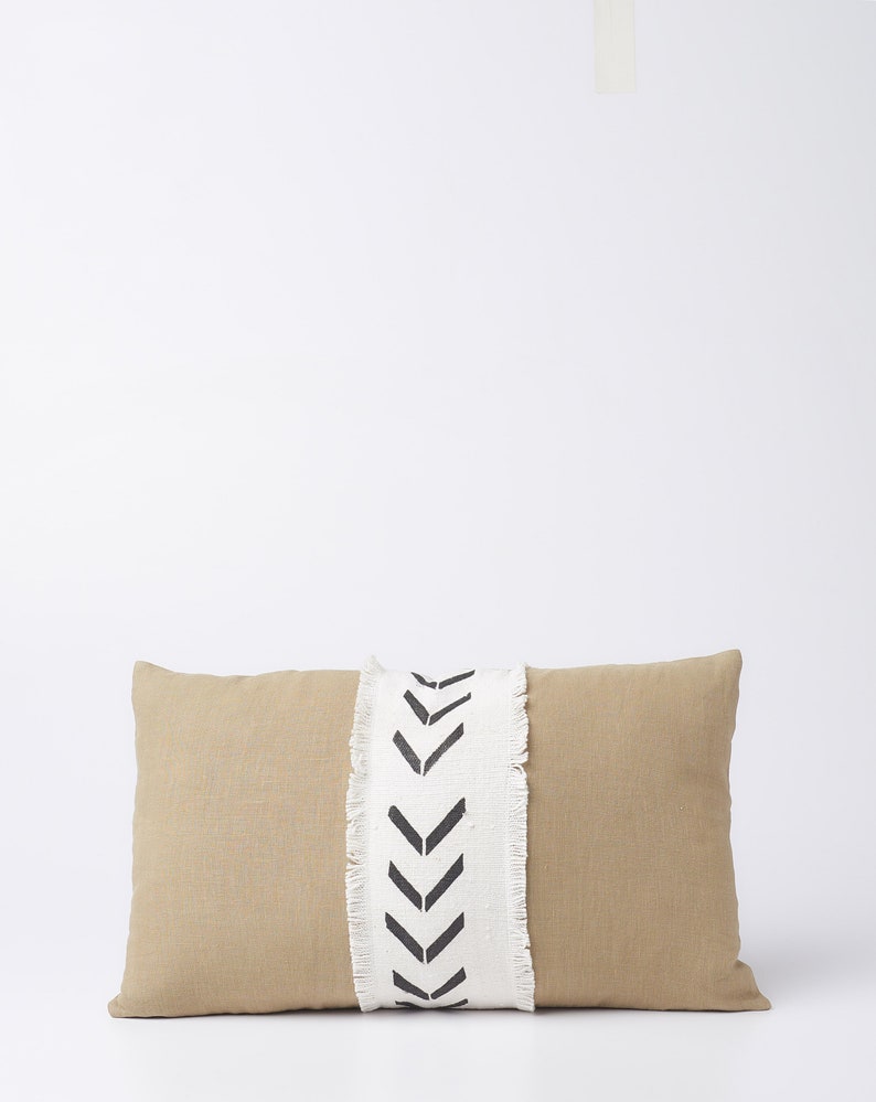 May include: A beige rectangular pillow with a white and black chevron pattern down the center. The pillow has a frayed edge.