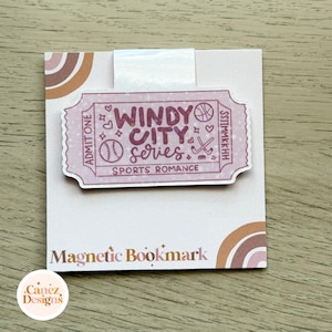 May include: A magnetic bookmark featuring a pink ticket-shaped design with the text Windy City Series Sports Romance. The bookmark includes illustrations of a basketball, baseball, and hockey sticks, set against a white backing card with arches.