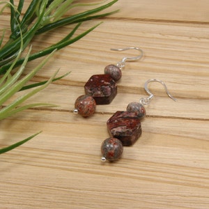 May include: A pair of silver earrings with red and brown jasper stone beads. The earrings feature a hexagonal bead, a round bead, and a smaller round bead.