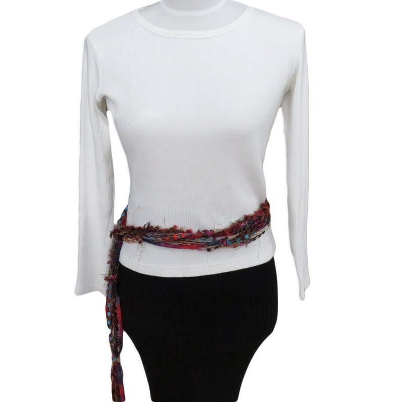 Peut inclure: Chemise blanche &agrave; manches longues avec une ceinture tiss&eacute;e color&eacute;e. La chemise a une texture c&ocirc;tel&eacute;e et un col rond.