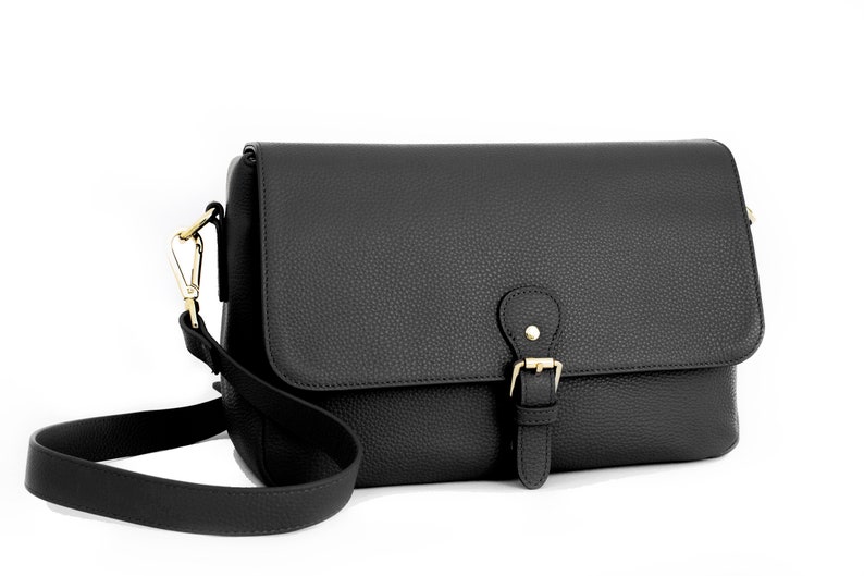May include: Black crossbody bag with a textured finish. The bag features a flap closure with a gold-colored buckle and a matching adjustable shoulder strap. The bag is designed with a rectangular shape.