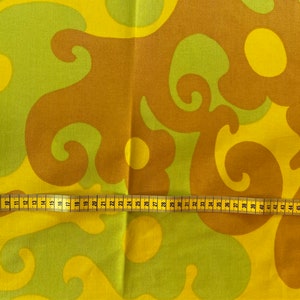 May include: A yellow and brown fabric with a swirling pattern. A yellow measuring tape is laid across the fabric.