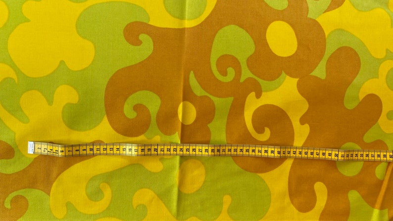 May include: A yellow and brown fabric with a swirling pattern. A yellow measuring tape is laid across the fabric.