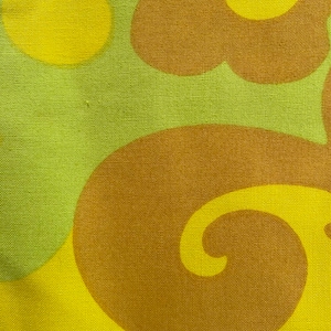 May include: Abstract fabric with a repeating pattern of brown and yellow swirls and circles. The fabric has a textured surface.
