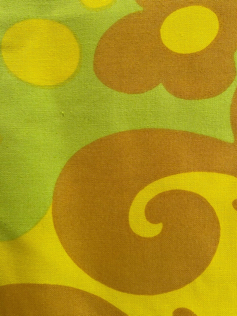 May include: Abstract fabric with a repeating pattern of brown and yellow swirls and circles. The fabric has a textured surface.
