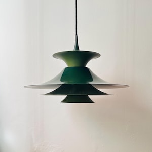 Może przedstawiać: Zielona, wielowarstwowa lampa wisząca o nowoczesnym designie. Lampa ma szereg nakładających się na siebie, talerzowych kloszy.