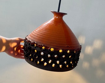 May include: A brown ceramic pendant light with a black, patterned, openwork bottom. The light has a round, bulbous shape and a simple, black cord.