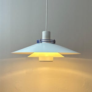 Könnte beinhalten: Weiße Pendelleuchte mit blauem Besatz am oberen Rand. Die Leuchte hat einen weißen Schirm mit einem kleineren weißen Schirm darunter.