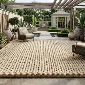 Puede incluir: Una gran alfombra beige de punto grueso domina una escena de patio al aire libre. Dos sillones con marcos met&aacute;licos y cojines neutros se colocan a cada lado. El fondo presenta un jard&iacute;n, un cenador y obras de arte.