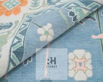 Könnte beinhalten: Aufgerollter Teppich mit floralem Muster in Blau-, Weiß-, Orange- und Grüntönen. Der Teppich hat ein detailliertes Design mit einem Rand und dem Text "RH STORES".