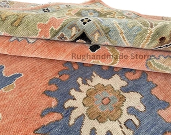 May include: Close-up of a folded rug with a detailed floral pattern. The rug features a colour palette of coral, blue, green, and beige. The text "Rughandmade Store" is visible on the rug.