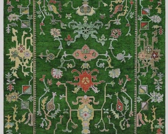 Op de afbeelding: Een groene rechthoekige vloerkleed met een ingewikkeld bloemen- en geometrisch patroon. Het vloerkleed heeft een centraal ontwerp met rode, gele en roze accenten, omgeven door een rand van zich herhalende motieven. Het vloerkleed heeft een handgemaakt uiterlijk.