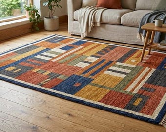 May include: A rectangular area rug with a geometric pattern in shades of red, blue, yellow, and green. The rug has a dark blue border and a fringed edge. The rug is placed on a hardwood floor.