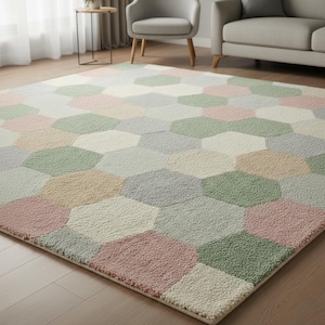 Può includere: Un grande tappeto con un motivo geometrico in tonalità pastello, tra cui rosa, verde, beige e grigio. Il tappeto è realizzato in un materiale morbido e strutturato ed è posizionato su un pavimento in legno. Il design presenta un motivo esagonale ripetuto.