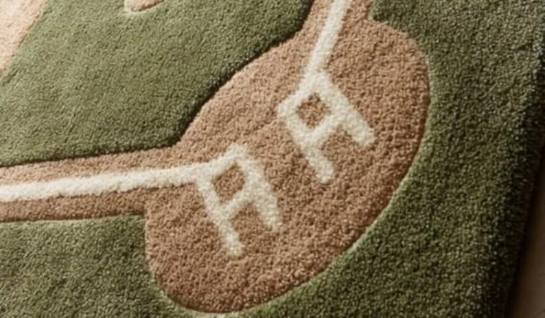 May include: A baseball-themed rug with a green field, tan infield, and white lines. The rug features the letters "RR" in white on the infield. The rug is made of a soft, textured material.