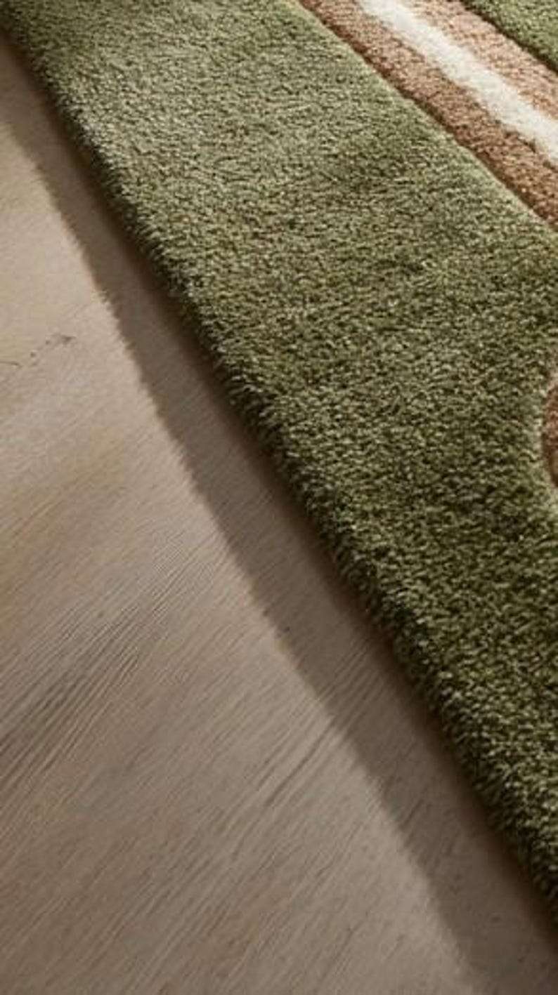 May include: A close-up of a green shag rug with a striped design in shades of beige and brown. The rug has a soft, textured appearance and is placed on a light-colored wooden floor.