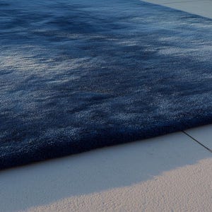 May include: A large, rectangular, plush rug in shades of blue. The rug has a soft, textured appearance and is placed on a light-colored tiled surface. The rug's color gradient creates a sense of depth and visual interest.