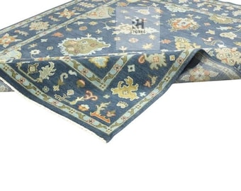 May include: A blue area rug with an intricate floral pattern. The rug features a dark blue field with a border in lighter blue and beige. The design includes floral and geometric elements, with a folded corner revealing the rug's backing.