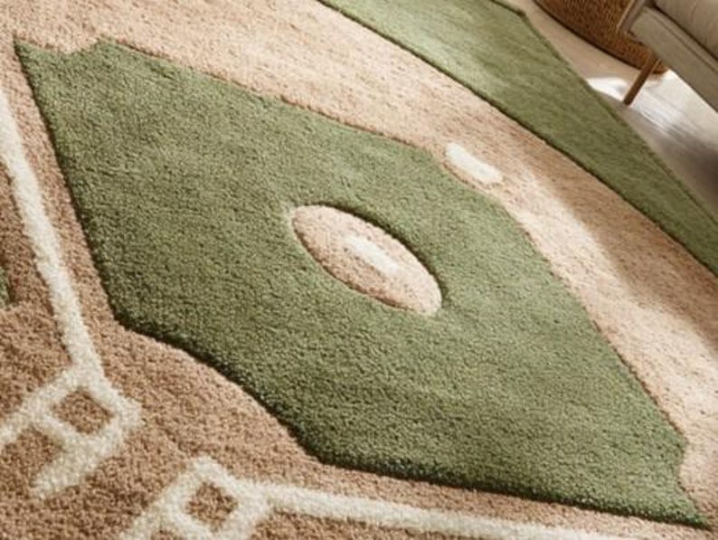 May include: Close-up of a large area rug with a geometric design. The rug features a diamond shape in olive green with a beige oval in the center. The background is beige with white geometric patterns.